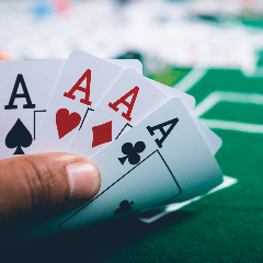 Image of a hand holding four aces of playing cards.