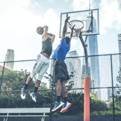 Image of a two people playing basketball on a playground in the city.