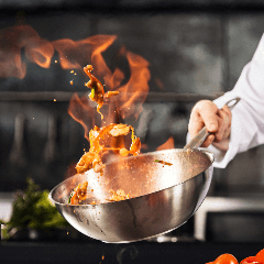 Image of a chef cooking with a pan over flames in a kitchen.