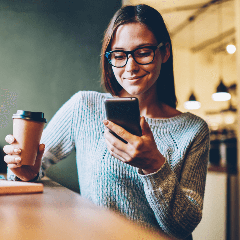 Image of a woman looking at a phone while enjoying a cup of coffee.