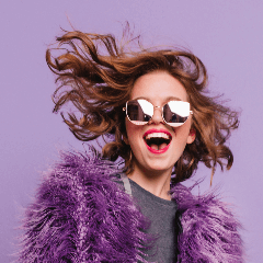 Image of a joyful, youthful woman sporting sunglasses and a stylish coat.