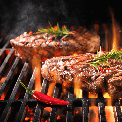 Image of two steaks sizzling on a flaming hot grill.