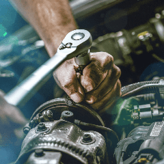 Image of a mechanic holding a wrench while working on a car engine.