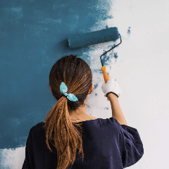 Image of a woman with a paint roller painting a wall.